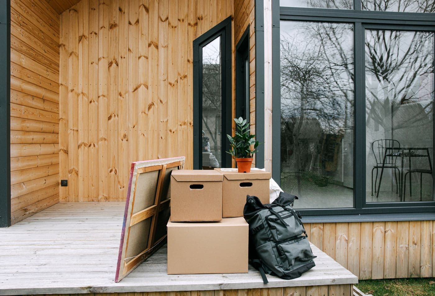 Cardboard deliveries beside a potted plant on a porch