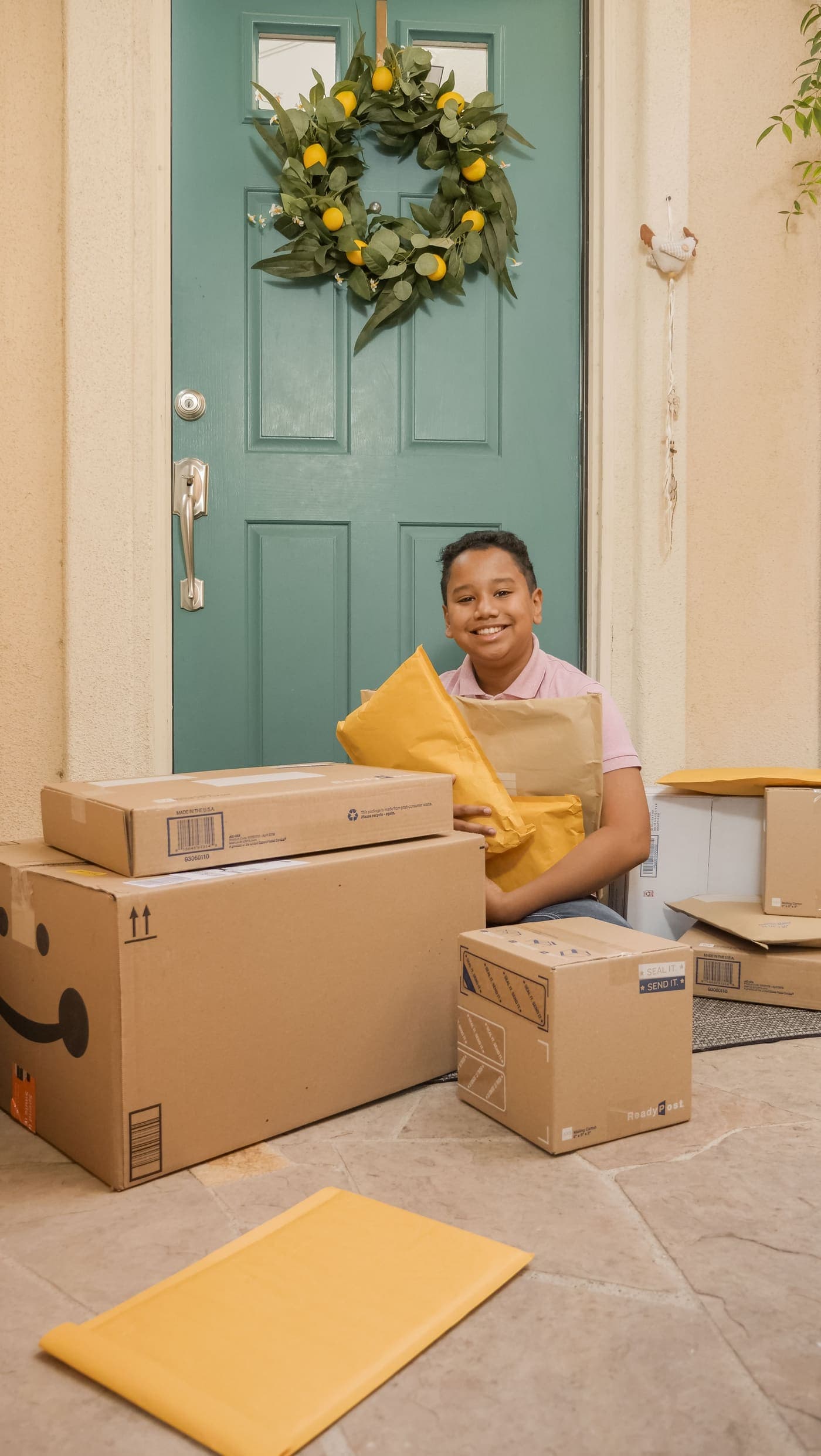 A smiling school-age boy on a porch surrounded by delivered packages